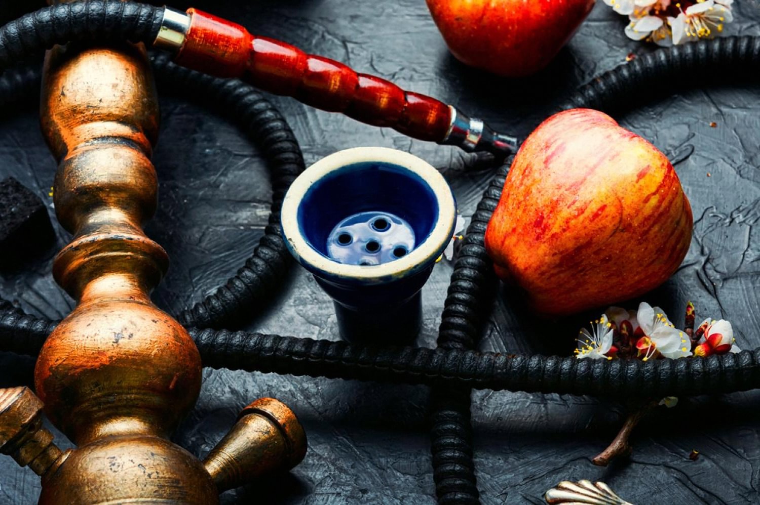 Traditional brass hookah with apple and blue clay bowl on dark stone surface
